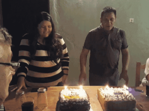a woman in a black and white striped sweater stands next to a man and two cakes with candles on them