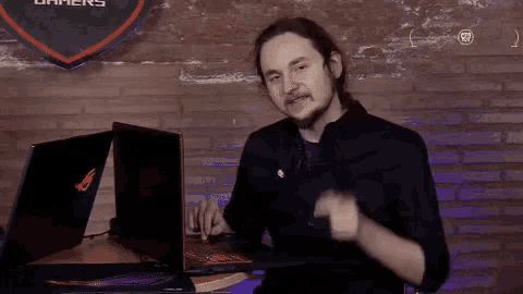a man sitting at a table with a laptop and a sign that says gamers on it