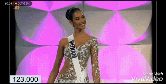 a woman wearing a sash that says vietnam is standing in front of a pink background .