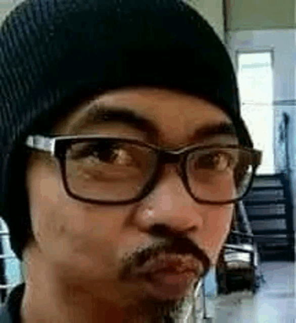a man with a beard and glasses is wearing a black beanie .