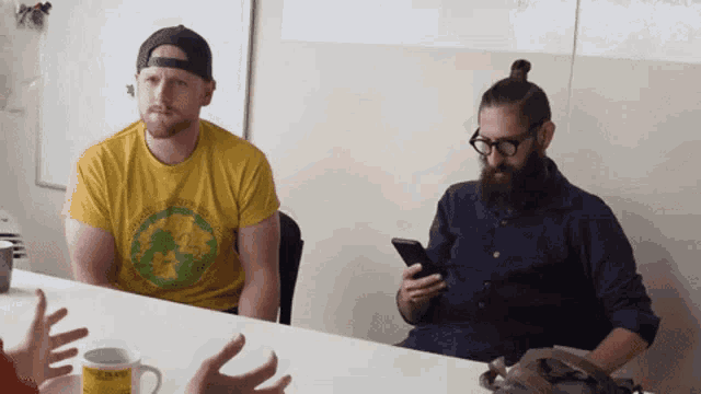 two men sitting at a table with one wearing a yellow shirt that says ' united states of america ' on the front