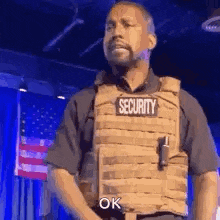a man wearing a security vest is standing on a stage and saying `` ok '' .