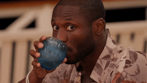 a man in a floral shirt drinks from a blue cup