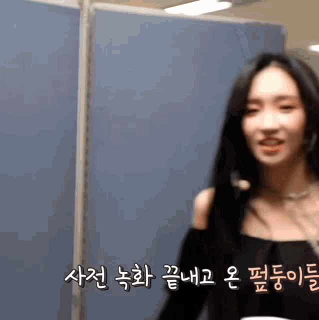 a woman with long black hair is standing in front of a blue wall with korean writing on it .