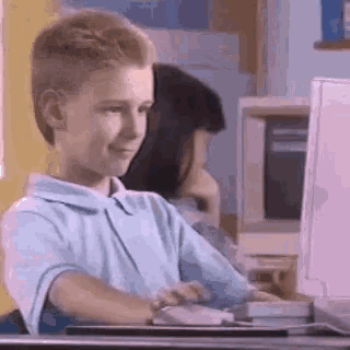 a young boy is sitting at a desk typing on a computer .