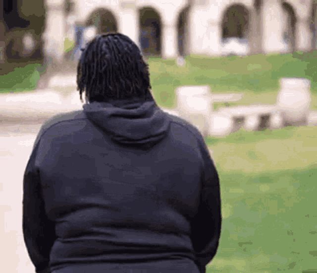 a man in a black hoodie is standing in front of a building in a park .
