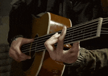 a person is playing an acoustic guitar with their left hand