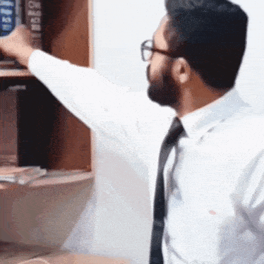 a man in a white shirt and black tie is reaching for a book on a bookshelf