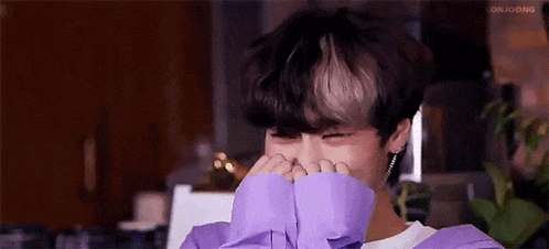 a young man is covering his face with his hands while wearing a purple shirt .