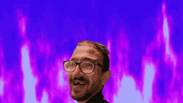 a man with glasses and a beard is smiling in front of purple flames