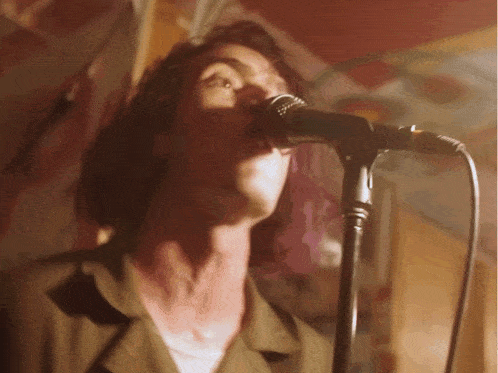 a man singing into a microphone with a painting on the wall behind him
