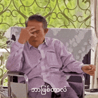 a man in a purple shirt is sitting in a chair with his hand on his face .