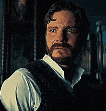 a man with a beard wearing a vest and a white shirt has his eyes closed