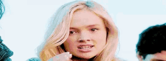 a close up of a woman with blonde hair making a funny face while standing next to a man .