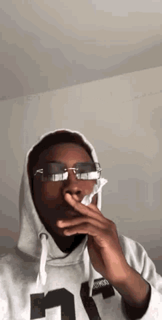 a man wearing a hoodie and sunglasses is blowing his nose with a napkin .