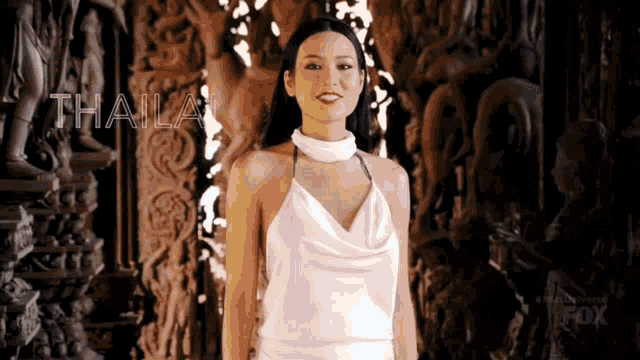 a woman in a white dress is standing in front of a statue and the word thailand is visible