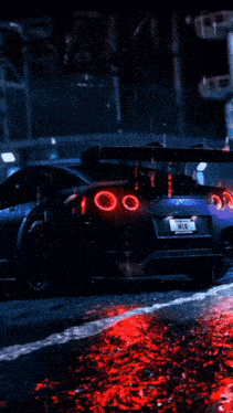 a black sports car with red lights on the hood is driving down a wet street at night .