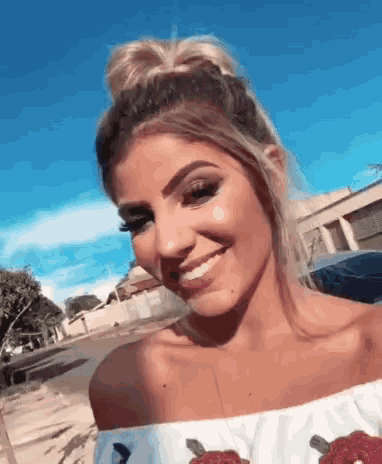 a woman wearing a white off the shoulder top smiles