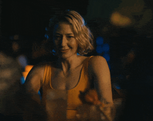 a woman in a yellow tank top sits at a table in the dark