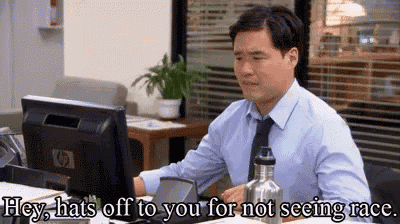 a man is sitting at a desk in front of a computer with the words `` hey hats off to you for not seeing race '' .