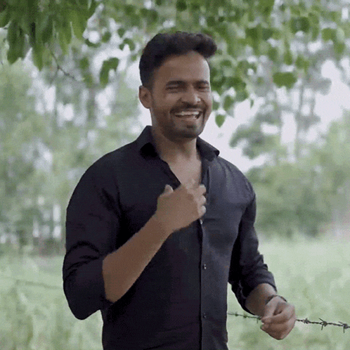 a man in a black shirt is standing in a field and smiling