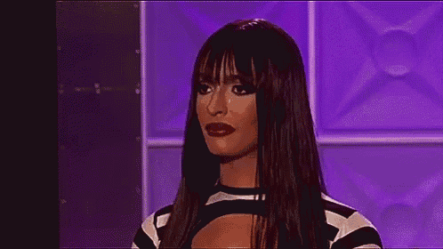 a woman with long black hair and red lips is standing in front of a purple wall and making a funny face .