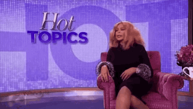 wendy williams is sitting in a pink chair in front of a hot topics sign