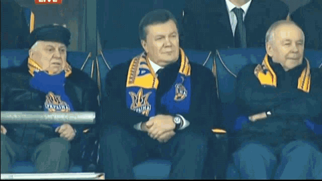 a man wearing a scarf that says ukraine sits in a stadium