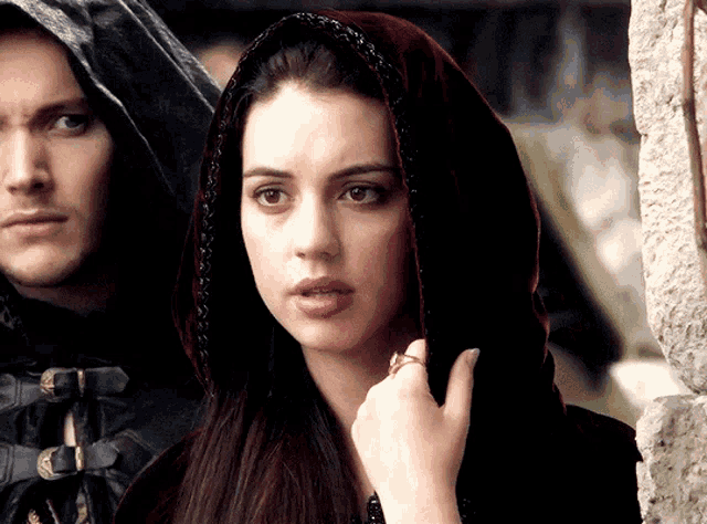 a woman wearing a hooded cape is standing next to a man wearing a hooded cape