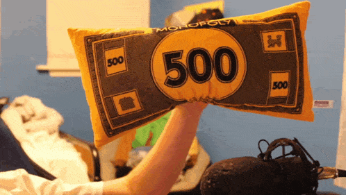 a person is holding a pillow that looks like a monopoly money