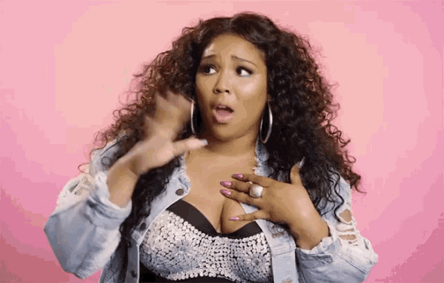 a woman with curly hair is wearing a denim jacket and a bra and is making a surprised face .