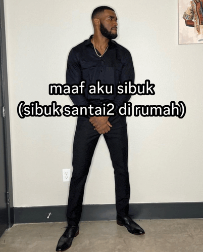 a man in a black suit is standing in front of a wall with a caption that says maaf aku sibuk