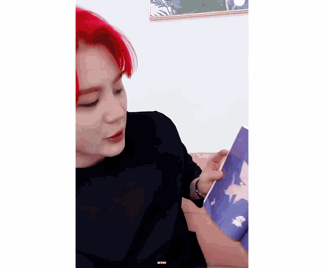 a man with red hair is reading a book with a cat on it .