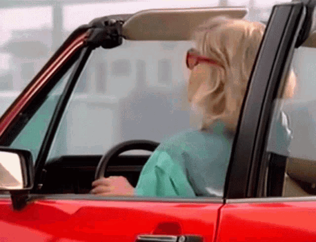 a woman is driving a red convertible with the top down