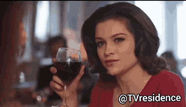 a woman in a red dress is holding a glass of wine in her hand