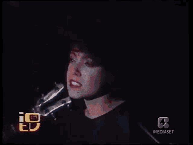 a woman is singing into a microphone in a dark room on a television show .
