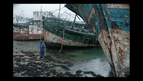 a man in a blue jumpsuit is standing next to a boat that says ' a ' on the front