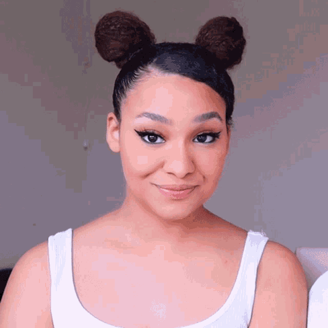 a woman wearing a white tank top has her hair in two buns