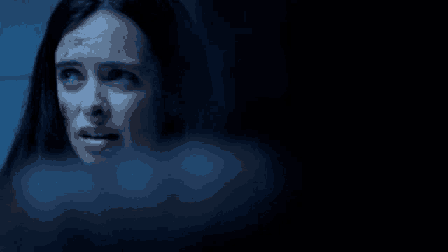 a woman with blood on her face looks at the camera in a dark room