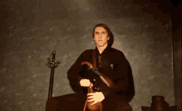 a man in a black jacket is playing a violin in a dark room