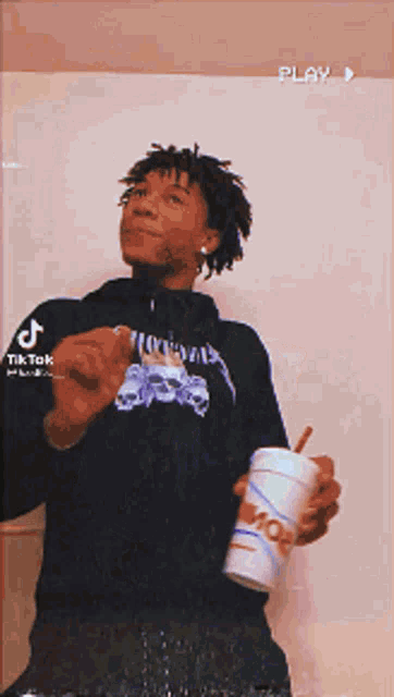 a young man in a black hoodie is holding a mcdonald 's cup with a straw