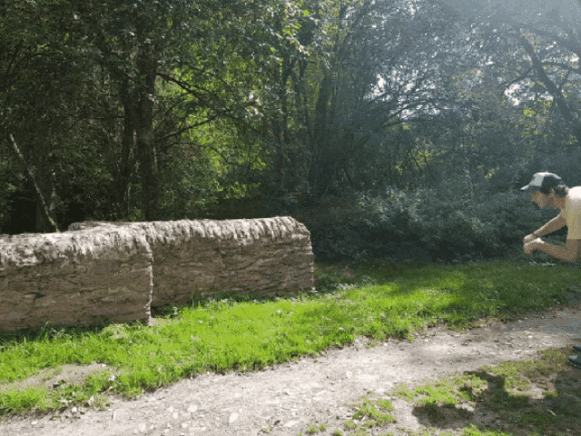 a man in a baseball cap looks at a stone wall in the grass