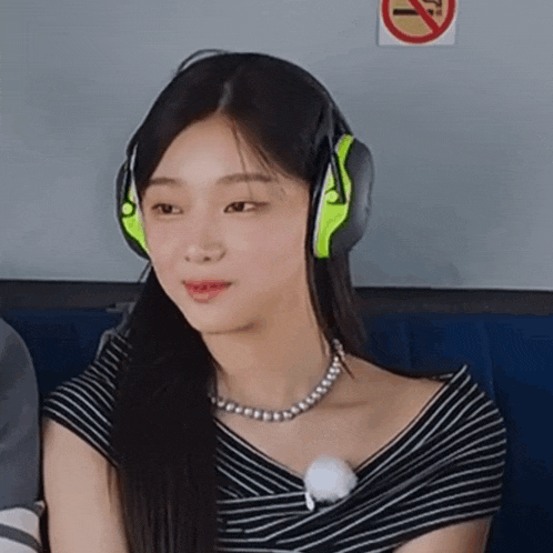 a woman wearing headphones and a pearl necklace is sitting in front of a no smoking sign