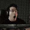 a man wearing headphones and glasses is raising his hands in the air in a dark room .
