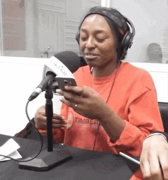 a woman wearing headphones and a red shirt is sitting in front of a microphone looking at her phone .