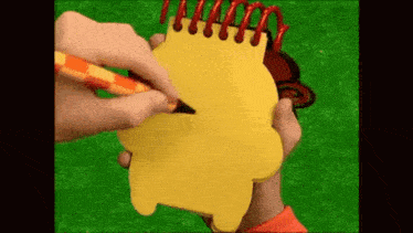 a person is writing on a yellow notebook with a red and orange pen
