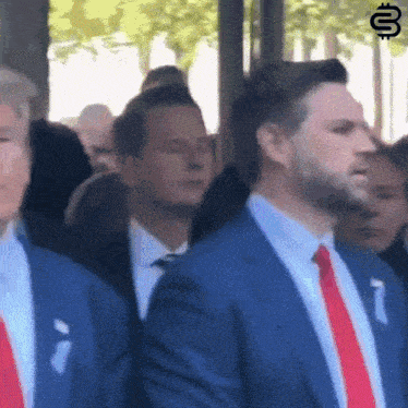 a man in a blue suit and red tie stands in a crowd of people