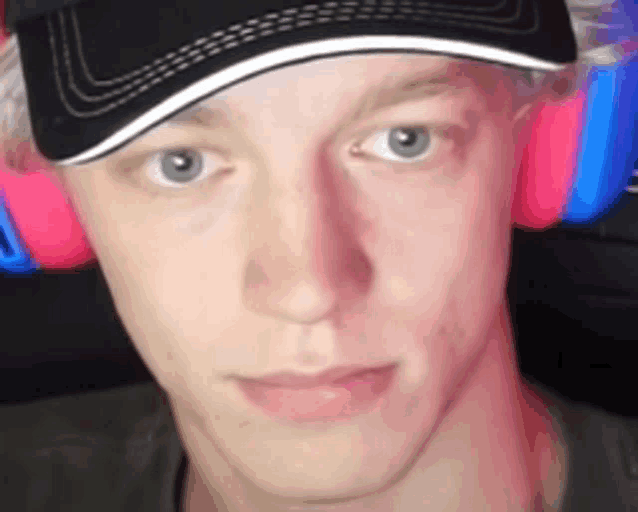 a young man wearing headphones and a baseball cap is looking at the camera .