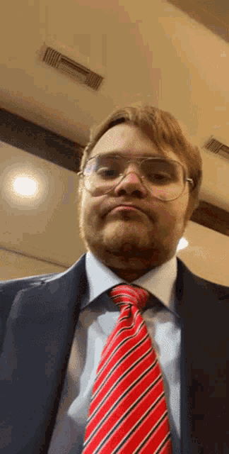a man wearing glasses and a red tie looks at the camera