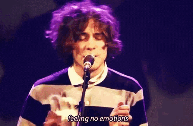 a man is singing into a microphone while wearing a striped shirt and purple hair .